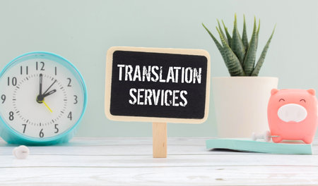 On a wooden table there are reports, a potted plant, a magnifying glass, a black pen and a notebook with the text TRANSLATION SERVICES. business conceptの写真素材