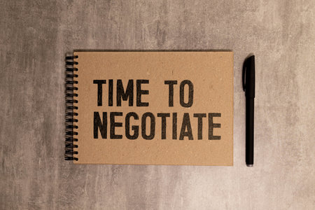 A business card with the text TIME TO NEGOTIATE lies on a wooden office table among office supplies.の写真素材