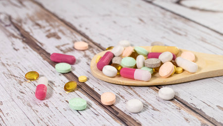 Vitamin capsules in a wooden spoon on a colored background. Pills served as a healthy meal. Drugs, pharmacy, medicine or medical healthycare concept.の写真素材