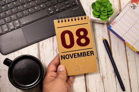 Calendar for November 8: name of the month in English, numbers 0 and 8 birch branch with one yellow leaf, fallen birch leaves on a wooden table, gray background, rays of the sunの写真素材