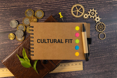 CULTURAL FIT text on craft colored notepad and green plant on the dark background.の写真素材