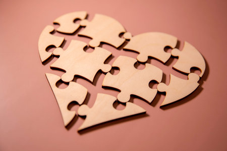 closeup of some separated pieces of a puzzle which together form a heart on a white rustic wooden surface, depicting the idea of rupture or cooperationの写真素材