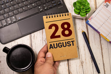 Wooden block calendar with the date August 28 and spikelets of wheat on a beige concrete background
