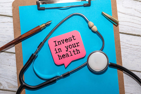 Healthy lifestyle, food and sport concept. Top view of Stethoscope measuring tape pink dumbbell, sport water bottles, fruit and note book with Invest in your health text on black background.の写真素材