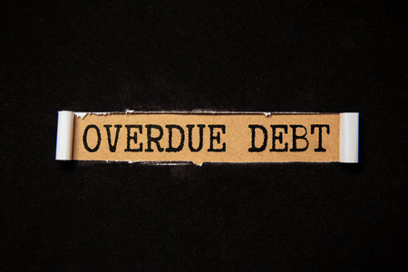 OVERDUE DEBT text on a sheet of notepad. Coins are scattered, pencils on a gray wooden background.の写真素材