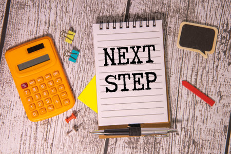 Close-up of a hand holding a black marker over an open notebook with NEXT STEPS text written on a white table. Planning and strategy concept.の写真素材