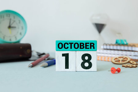 Wooden calendar with the date October 18 on desktop with laptop.の写真素材