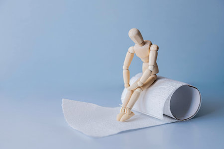figure of a man sitting on a roll of toilet paper holding his stomachの写真素材