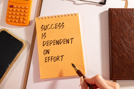 A person holding a stack of books and a piece of paper that says Success is dependent on effort.の写真素材
