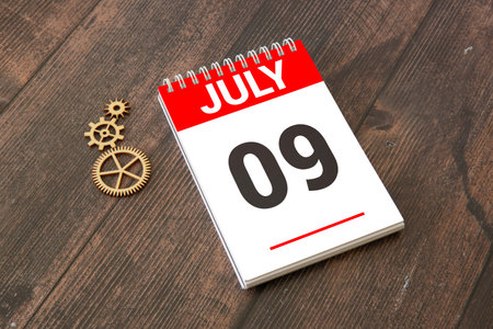 Female Hand holding wooden block calendar with the date July 9 on beige background