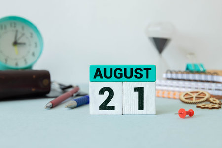 Wooden block calendar with the date August 21 and spikelets of wheat on a beige concrete background
