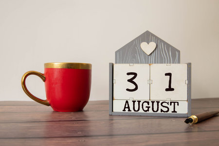Wooden block calendar with the date August 31 and spikelets of wheat on a beige concrete background