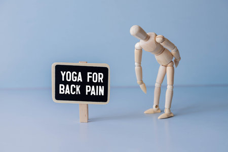 Rear view of a toned young woman with back pain standing against wall in fitness studioの写真素材