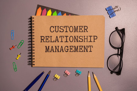 CRM Customer Relationship Management text on paper notebook page with alarm clock and calculator on wooden backgroundの写真素材