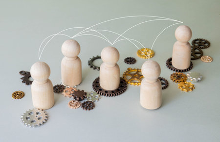 Wooden people figures as workers on connected gears. Teamwork and business communication concept.
