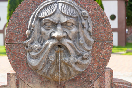 Rome, Italy - April 20th 2025 - Old stone fountain with sculpted face mask spouting water against brick wall.の写真素材