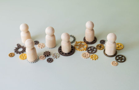 A conceptual image with wooden figures standing on interconnected gears. Teamwork, collaboration, and the interconnected nature of work concept.の写真素材