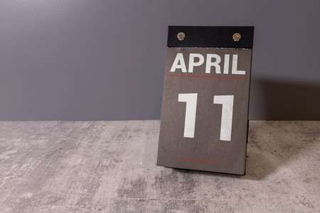 Minimalist yellow wooden block perpetual date calendar displaying APRIL 11 with light grey...