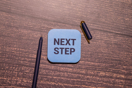Next steps phrase on notebook with pen and green plant on a white background .