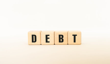 Wooden block with the word debt written on it. The block is placed on top of a red and white American flag. The flag is spread out, covering a large portion of the backgroundの写真素材