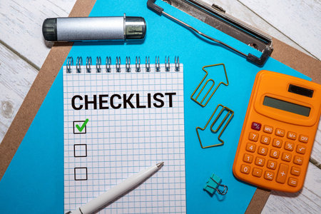 Hand checks quality control checklist box with pen on desk near laptop
