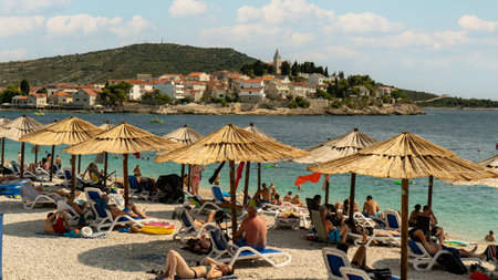 Primosten Croatia July 30, 2024, Idyllic Beach on Mediterranean Sea Coast Near Medieval Primosten City in Croatia. Summer Holidays Travel Destination Tourists Sunbathing and Enjoying Mala Raduca Beachの写真素材