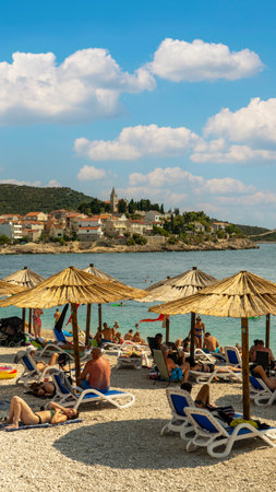 Primosten Croatia July 30, 2024, Idyllic Beach on Mediterranean Sea Coast Near Medieval Primosten City in Croatia. Summer Holidays Travel Destination Tourists Sunbathing and Enjoying Mala Raduca Beachの写真素材