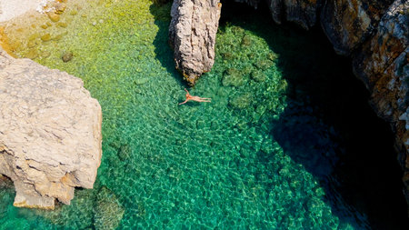 Beautiful Young Woman in Bikini Swims in Stara Baska Beach Krk Island, Croatia. Mediterranean Summer. Aerial Shot From Above. Blue Sea the Rocks Mountains and Coastline Calm Sea With Clear Blue Waterの写真素材