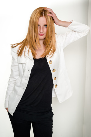 Portrait of beautiful young blond woman in white jacket and black shirt leaning against wall, isolated on white backgroundの写真素材