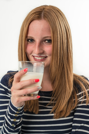 Smiling young girl drinking a glass of milk on a white backgroundの写真素材