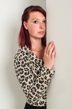 Young shy red-haired woman looking around the corner, fashion, tiger look, on white backgroundの写真素材