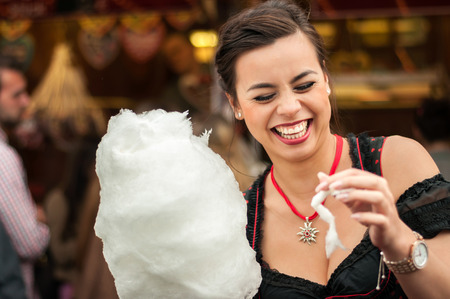 Beautiful young smiling woman wearing a traditional Dirndl dress with cotton candy floss at the Oktoberfest.の写真素材