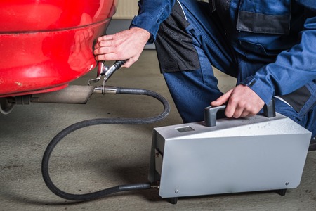 A diagnostic sensor is applied to the ehaust of a red car, measuring the composition and substances in the exhaust fumes in a garageの写真素材
