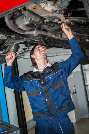 Portrait of a mechanic checking the condition a lifted red carの写真素材