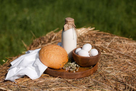 Milk, bread, eggs, napkin and wooden tray on haystack. Green grass background. Summer and sunshine.の写真素材