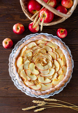 Round apple pie and red apples on brown backgroundの写真素材