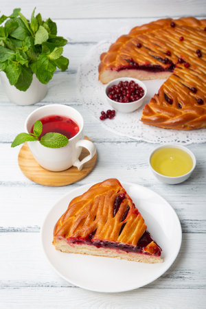 A piece of round cranberry pie, mint, honey and tea on white wooden backgroundの写真素材