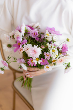 Woman in white dress holding beautiful bouquets of pink cosmos flowers. Hands with bouquets of seasonal flowers. Pink cosmos summer flowers. Wedding bouquet.の写真素材
