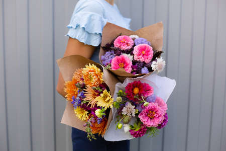 Woman in blue blouse holding beautiful bouquets of flowers. Hands with bouquets of seasonal flowers in craft paper. Bouquets as a gift. Orange and pink dahlia flowersの写真素材
