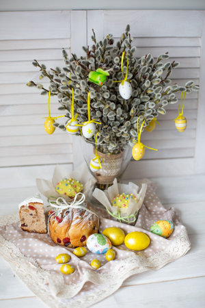 Easter yellow eggs, cakes and willow on white wooden background.