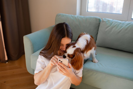 Young woman sitting at home with Cavalier King Charles Spaniel dog and phone.の写真素材