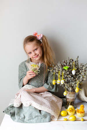The girl sitting on a table with Easter decor: cakes, eggs and bouquet of willow in a vase on the table.の写真素材