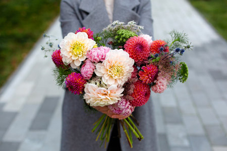 A person in grey coat holding beautiful bouquet of autumn flowers.の写真素材