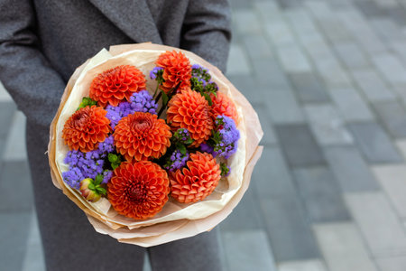 A person in grey coat holding beautiful bouquet of orange dahlia flowers.の写真素材