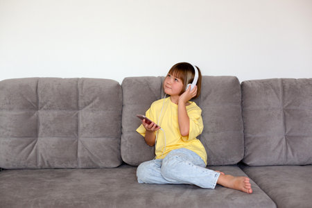 Girl of 8 years old in a yellow t-shirt and blue jeans with phone and headphones.の写真素材
