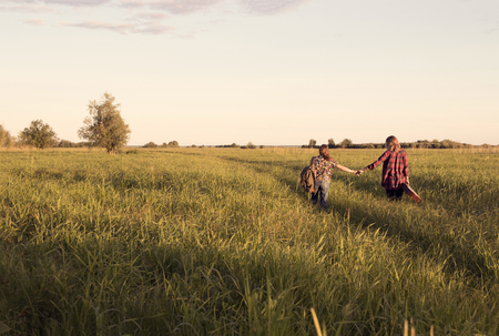 a couple of girls go on a dirt road on the big field with tall grassの写真素材