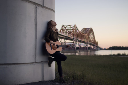 girl with a guitar standing at the foot of the bridge over the riverの写真素材