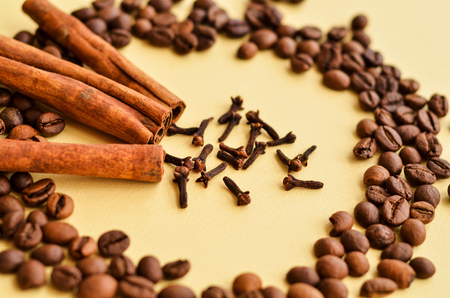 coffee beans in a circle with cinnamon and clove on a yellow background with a place under the textの写真素材