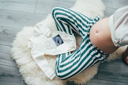 A pregnant woman hands her abdomen and sonogram image and baby clothersの写真素材