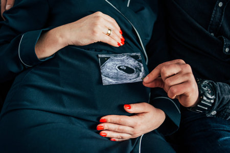 a woman holds ultrasound picture. A pregnant woman hands her abdomen